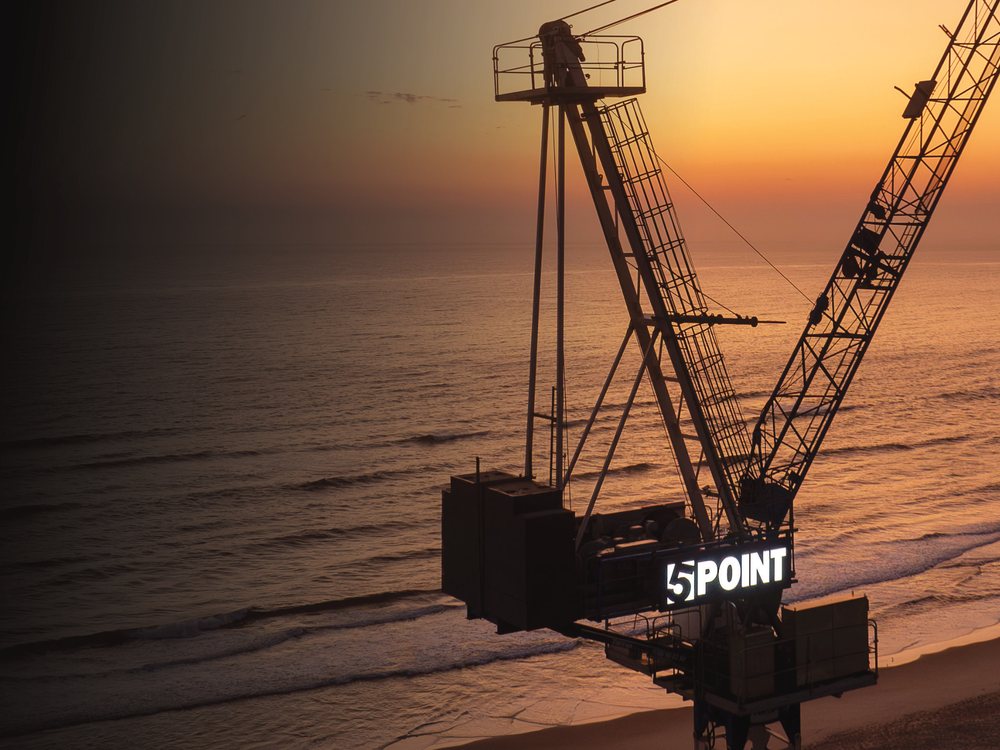 Tower crane with a lit company sign at sunset over the ocean